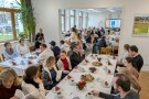 Studierende und Lehrkräfte sitzen gemeinsam an Tischen mit festlicher Dekoration zusammen.